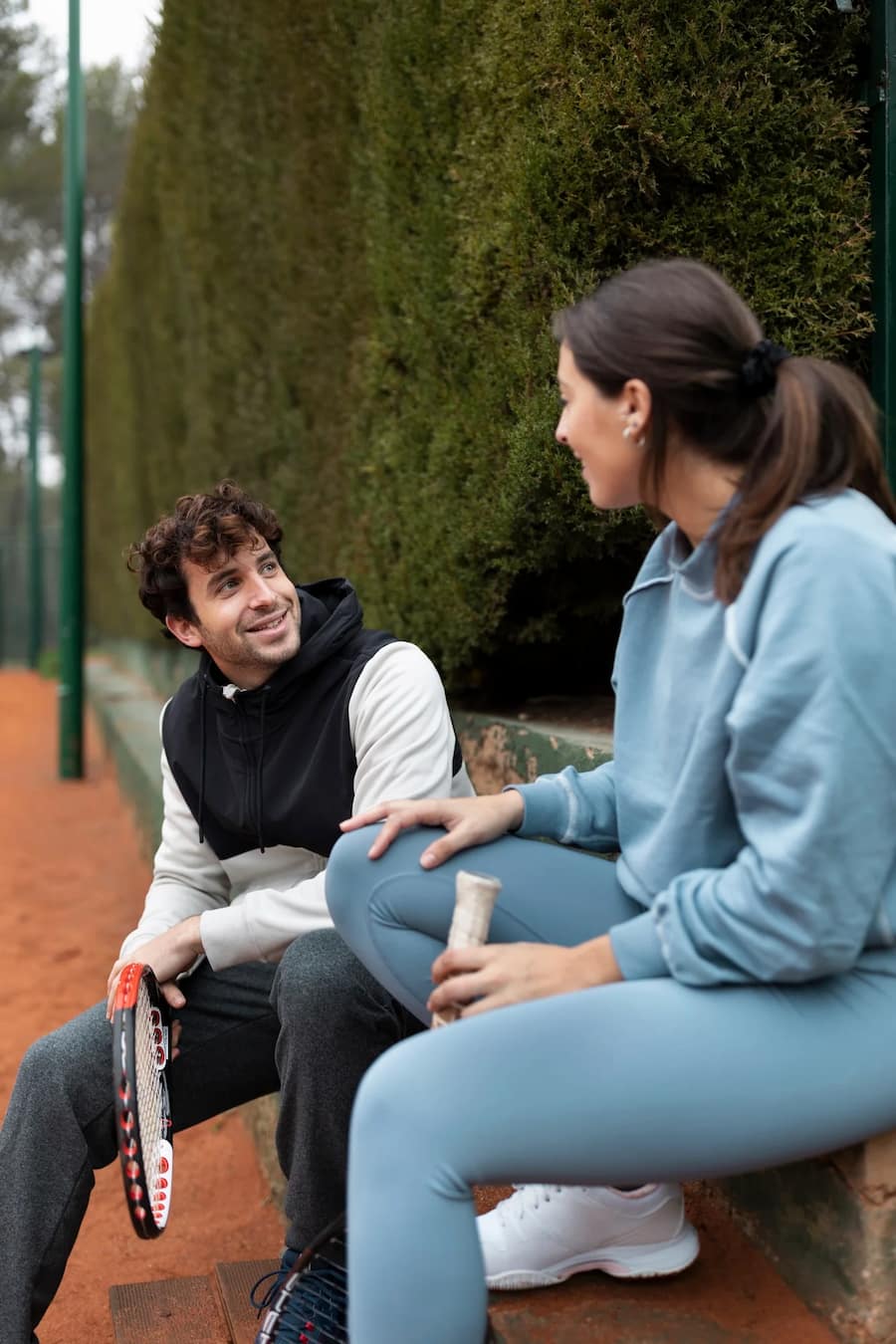 Man and woman speaking about their mental health, smiling with tennis rackets